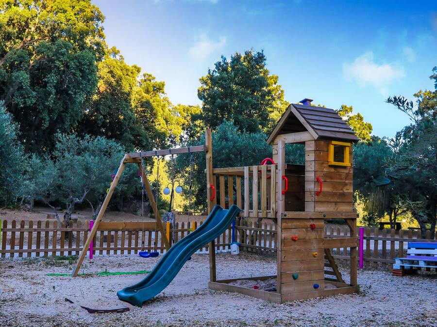 A playground with a slide, climbing structures, and a small wooden house.