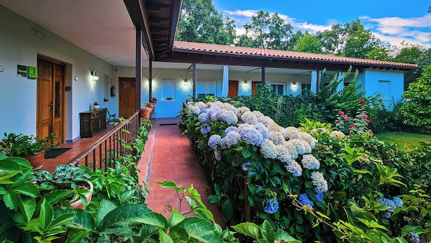 A hotel with a covered porch, potted plants, and a garden with hydrangeas. - Hotel Rural El Retiro de San Pedro (Arenas de San Pedro)