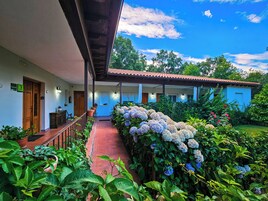Un hotel con un porche cubierto, plantas en macetas y un jardín de hortensias.