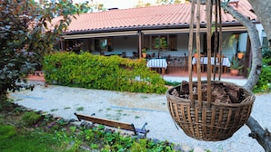 A rustic outdoor area with a wooden bench, a hanging basket, and a building with a tiled roof in the background. - Hotel Rural El Retiro de San Pedro (Arenas de San Pedro)