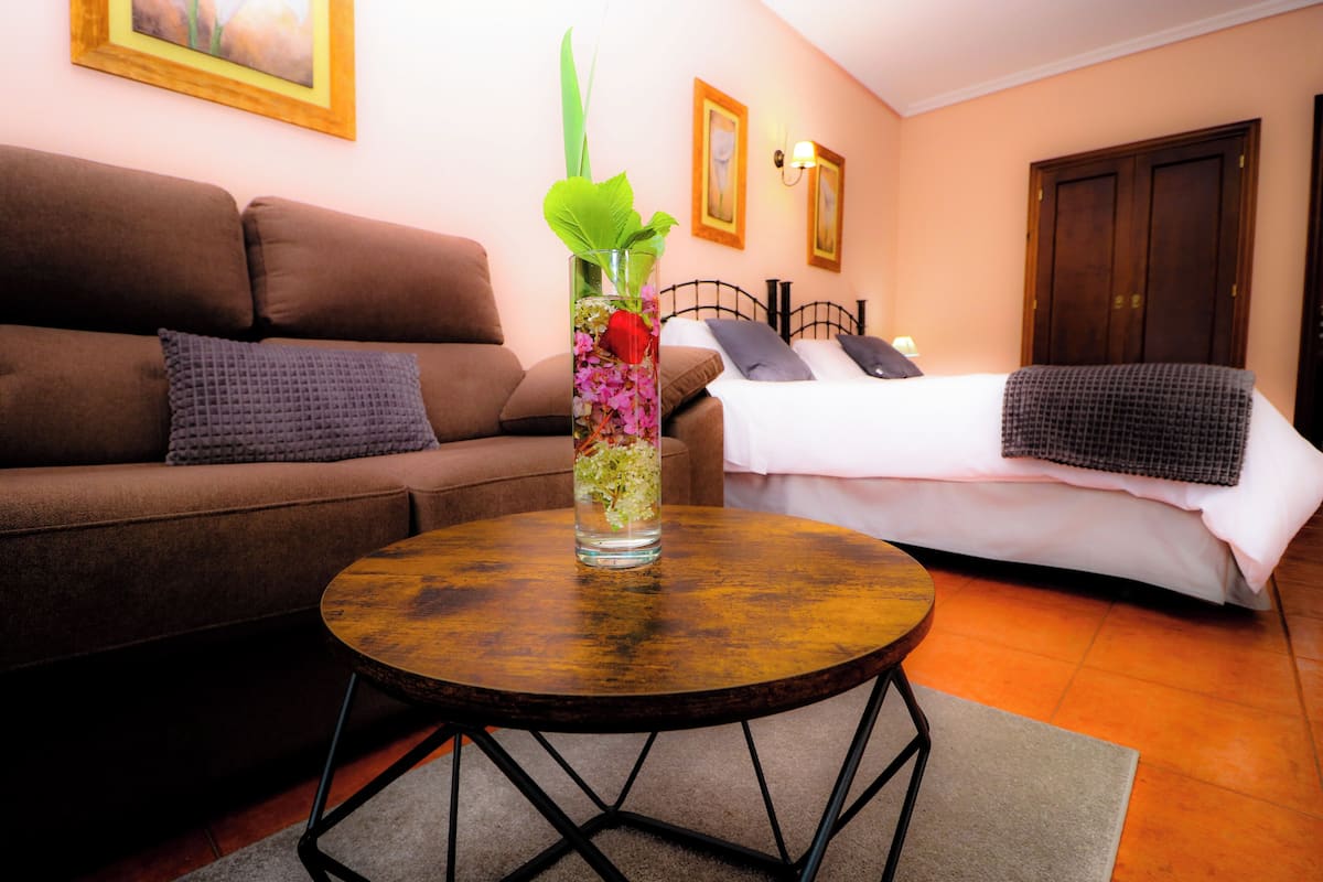Ein Wohnzimmer mit einem braunen Sofa, einem runden Holztisch und einem Bett mit weißer Bettwäsche.