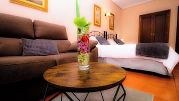 Una sala de estar con un sofá marrón, una mesa de centro redonda de madera y una cama con ropa de cama blanca.