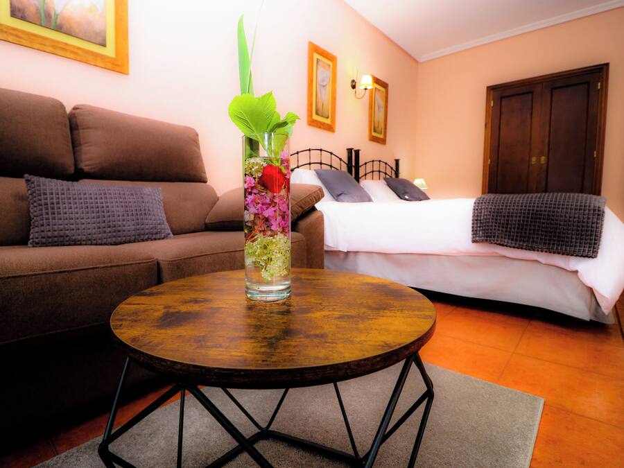 Una sala de estar con un sofá marrón, una mesa de centro redonda de madera y una cama con ropa de cama blanca.