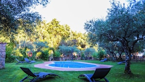 A backyard with a circular pool, surrounded by grass and trees. There are lounge chairs and a red circular decoration. - Hotel Rural El Retiro de San Pedro (Arenas de San Pedro)