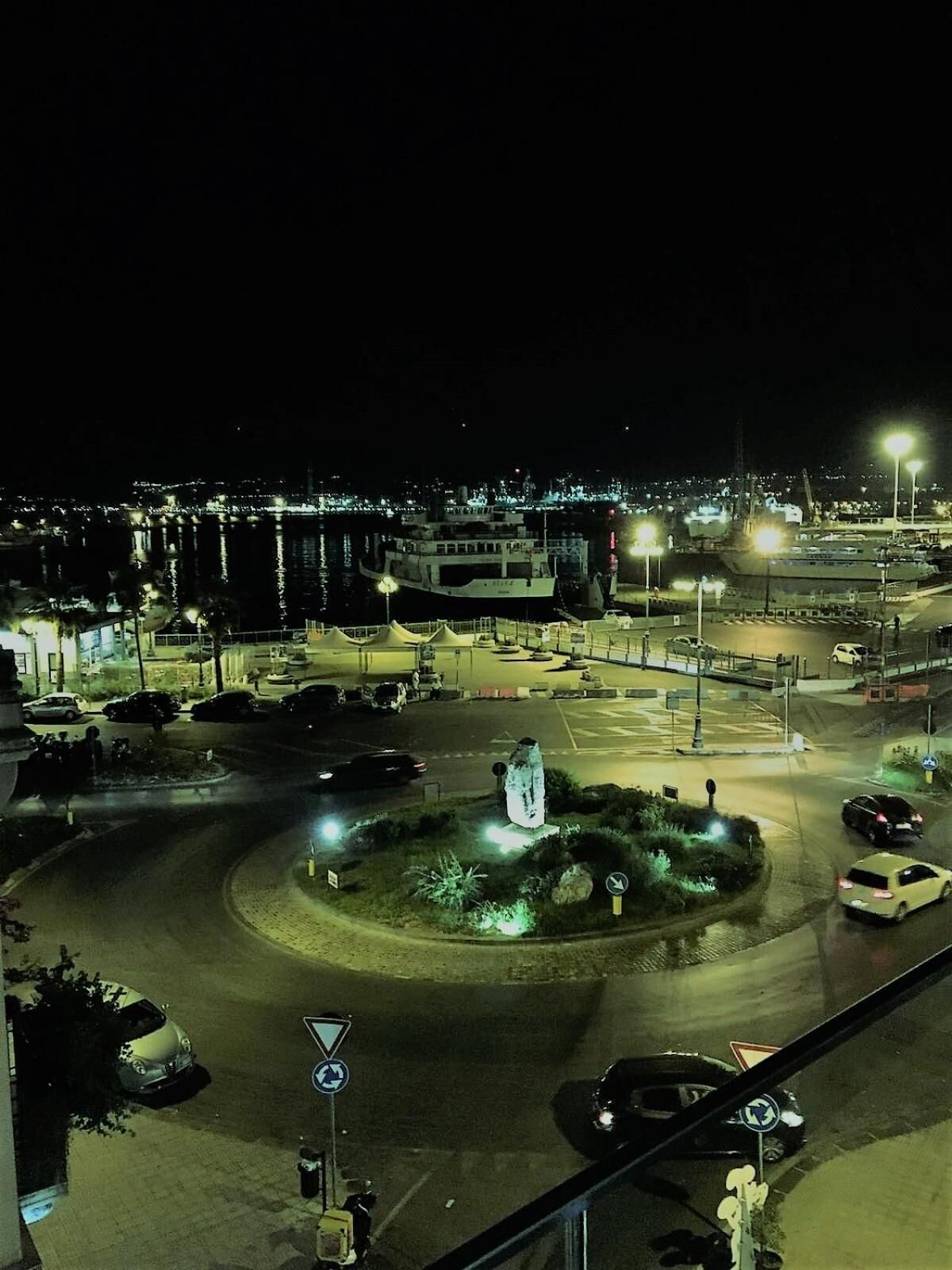 A nighttime view of a roundabout with cars and a large ship docked nearby.