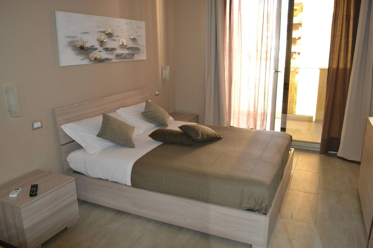 A neatly made bed with a wooden headboard, a bedside table with a remote control, and a wall-mounted artwork.