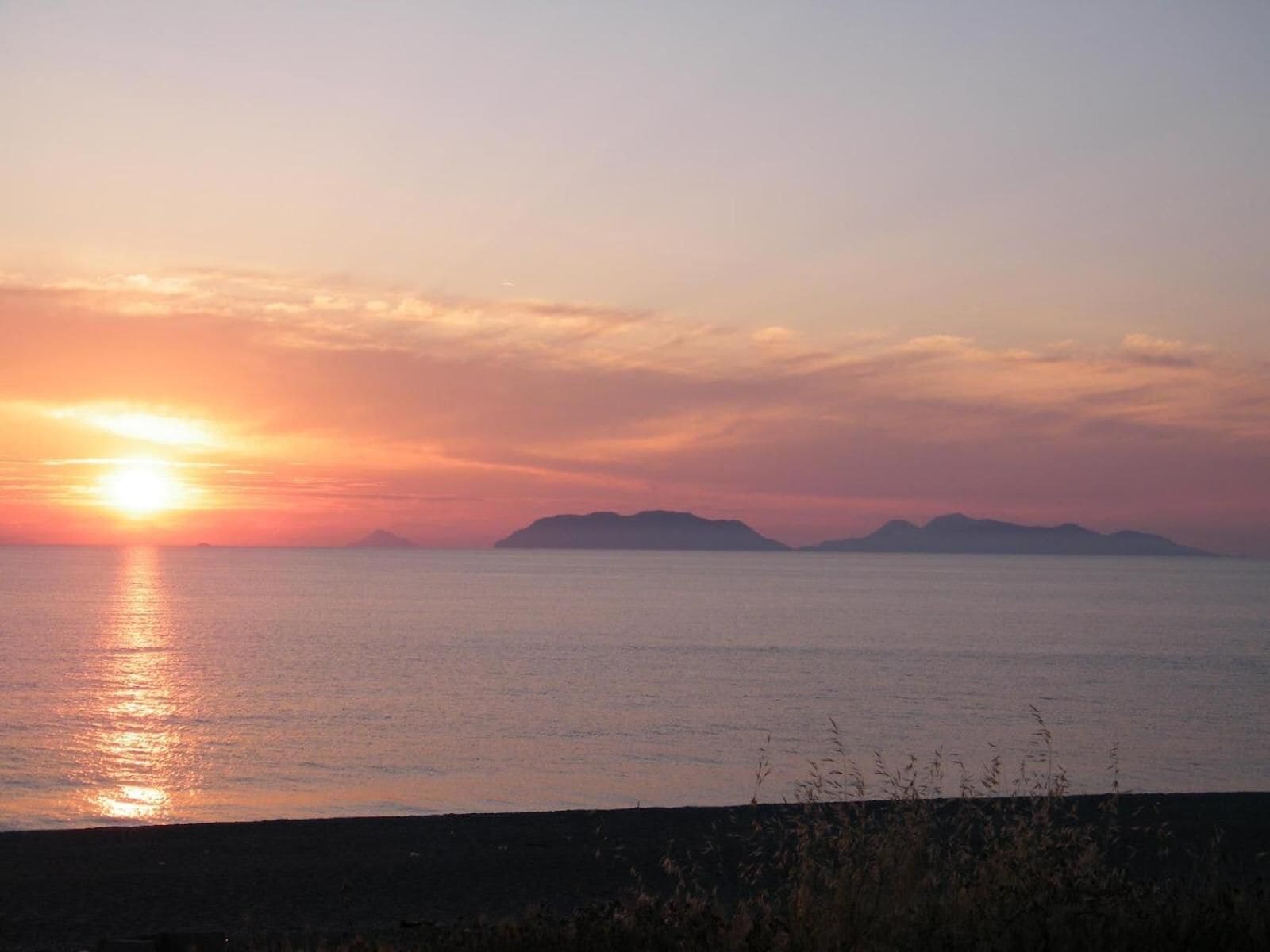 Ein Sonnenuntergang über ruhigem Meer mit fernen Landformen.
