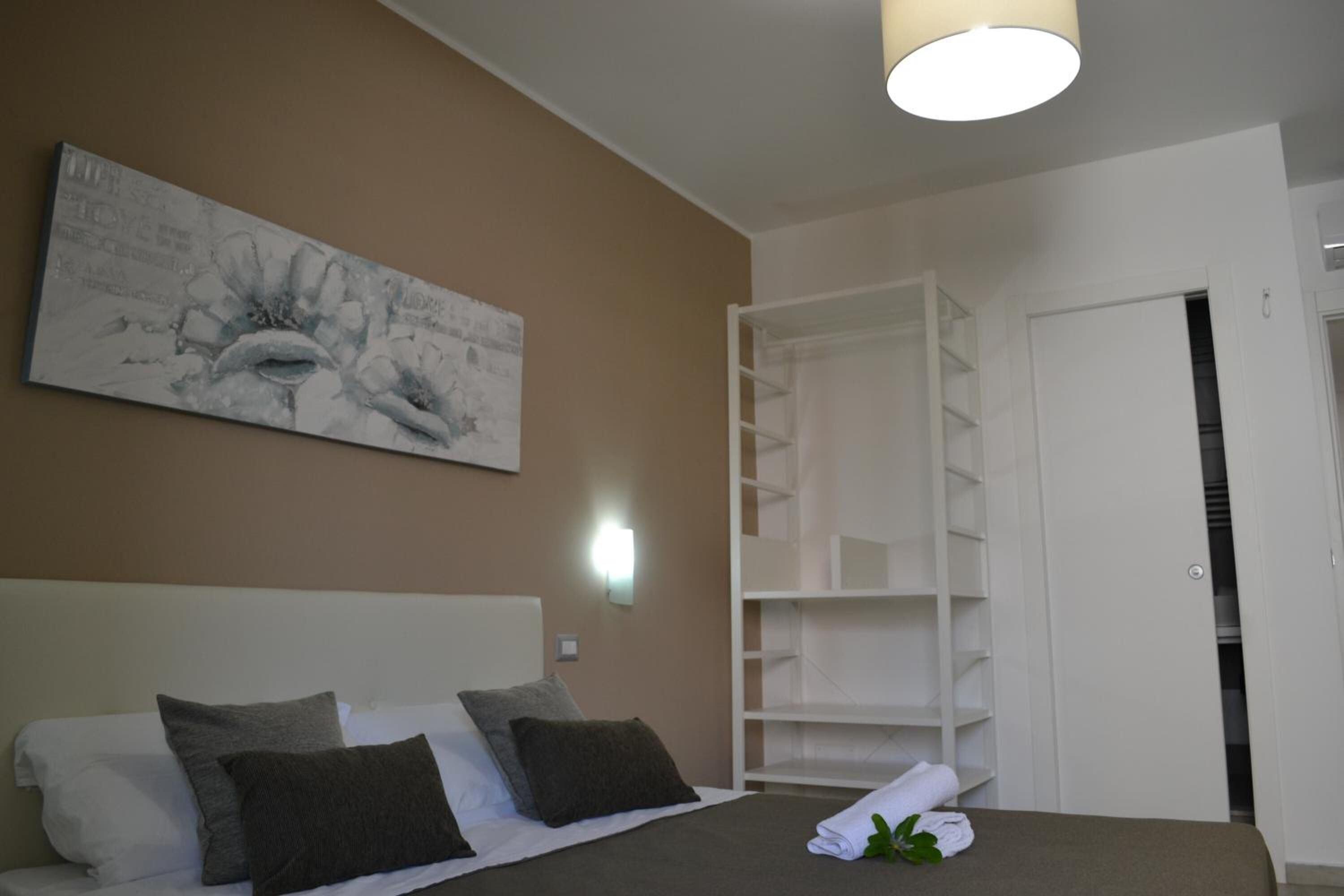Habitación de hotel con una cama, un cuadro abstracto grande en la pared, un armario blanco y una estantería blanca.