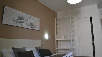 Habitación de hotel con una cama, un cuadro abstracto grande en la pared, un armario blanco y una estantería blanca.