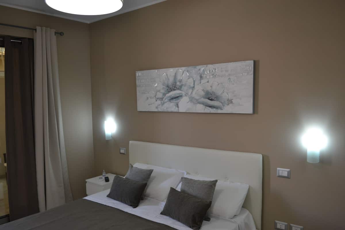 A hotel room with a bed, a nightstand, a wall-mounted light, and a painting.