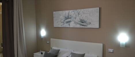 Habitación de hotel con cama, mesita de noche, luz de pared y un cuadro.