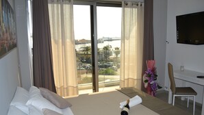 Habitación de hotel con cama, escritorio, silla, televisor y vista al puerto deportivo.