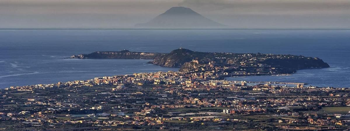 Un paisaje urbano costero con una colina destacada al fondo.