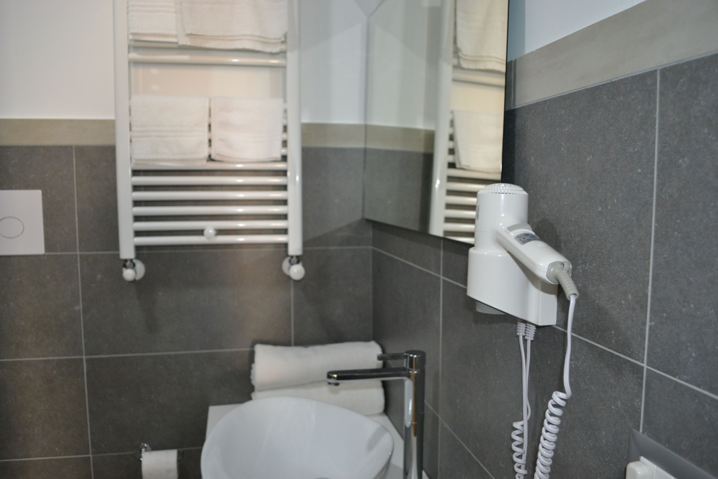 Une salle de bain avec des toilettes blanches, un porte-serviettes avec des serviettes pliées, un sèche-cheveux fixé au mur et un distributeur de serviettes.