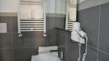 Une salle de bain avec des toilettes blanches, un porte-serviettes avec des serviettes pliées, un sèche-cheveux fixé au mur et un distributeur de serviettes.