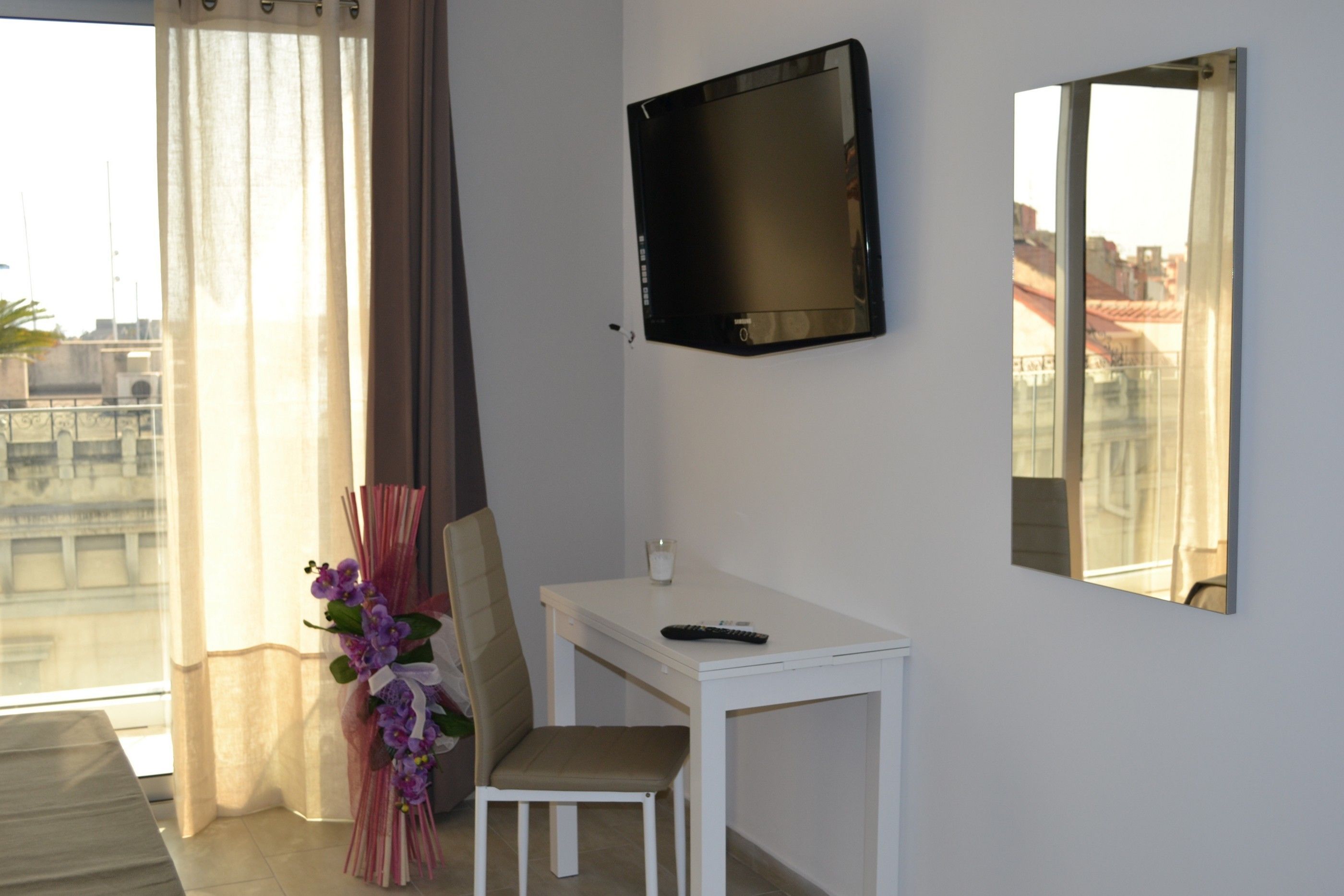 A room with a white desk, a chair, a TV mounted on the wall, and a large mirror.