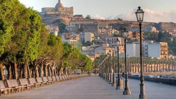 Un chemin piétonnier, bordé de bancs et de lampadaires, mène à un bâtiment historique surmonté d’un dôme.
