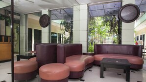 A lobby with a seating area consisting of a sofa and ottomans, a coffee table, and a large mirror. - RedDoorz near Juanda International Airport (Sidoarjo)