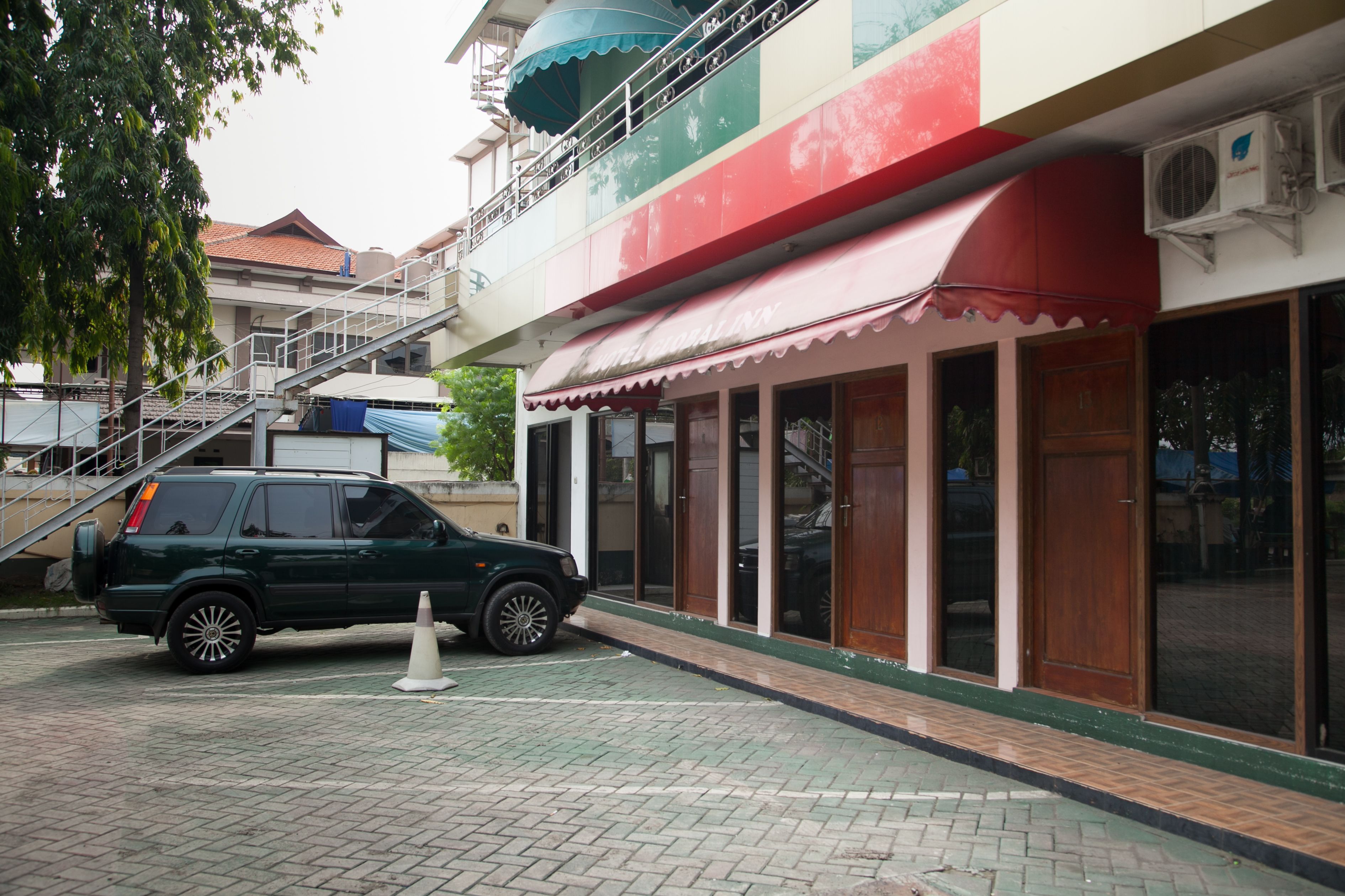 A hotel with a red and white awning, a staircase leading to a balcony, and a parked SUV.