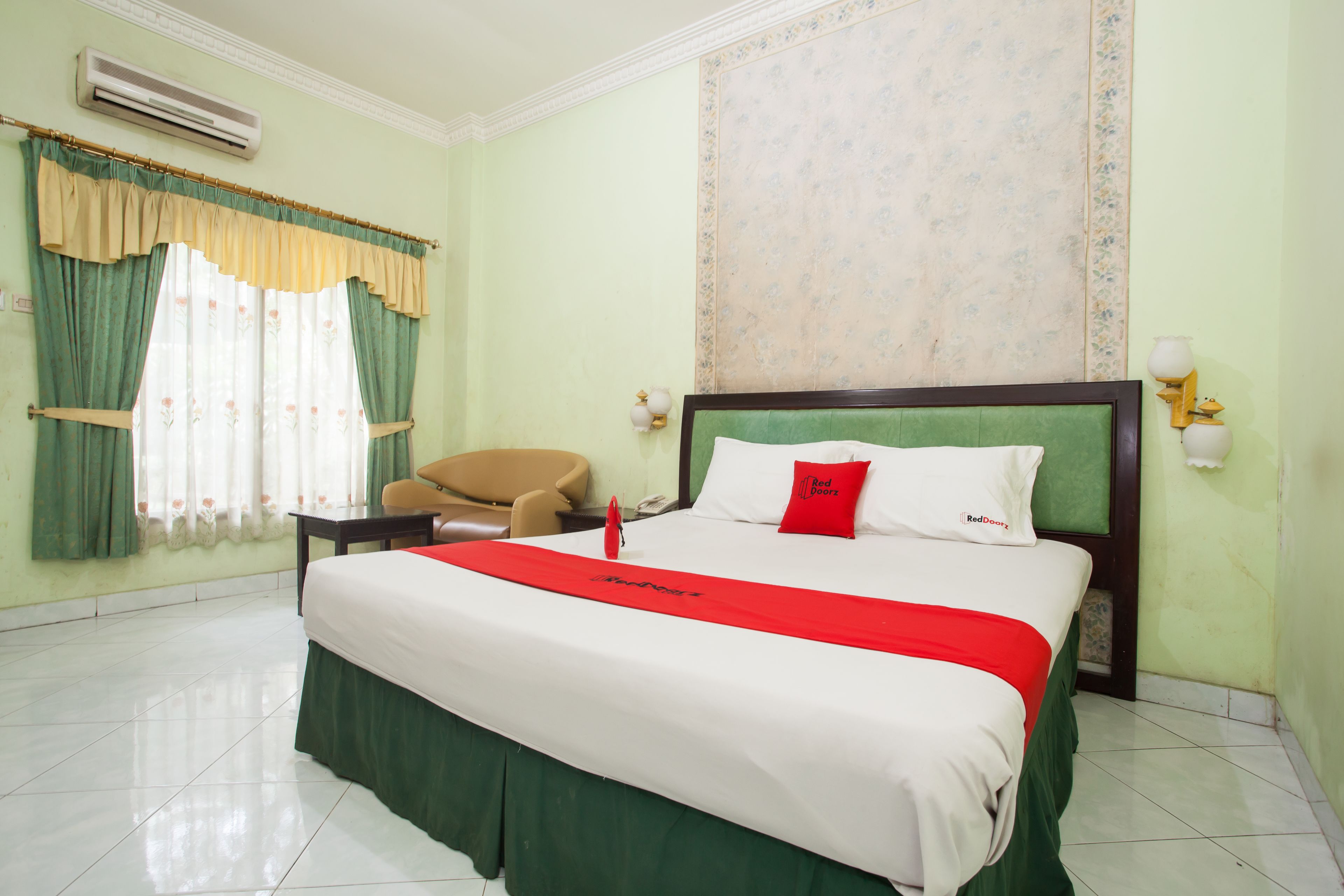 Habitación de hotel con una cama grande, una silla, un escritorio y un ventanal con cortinas.