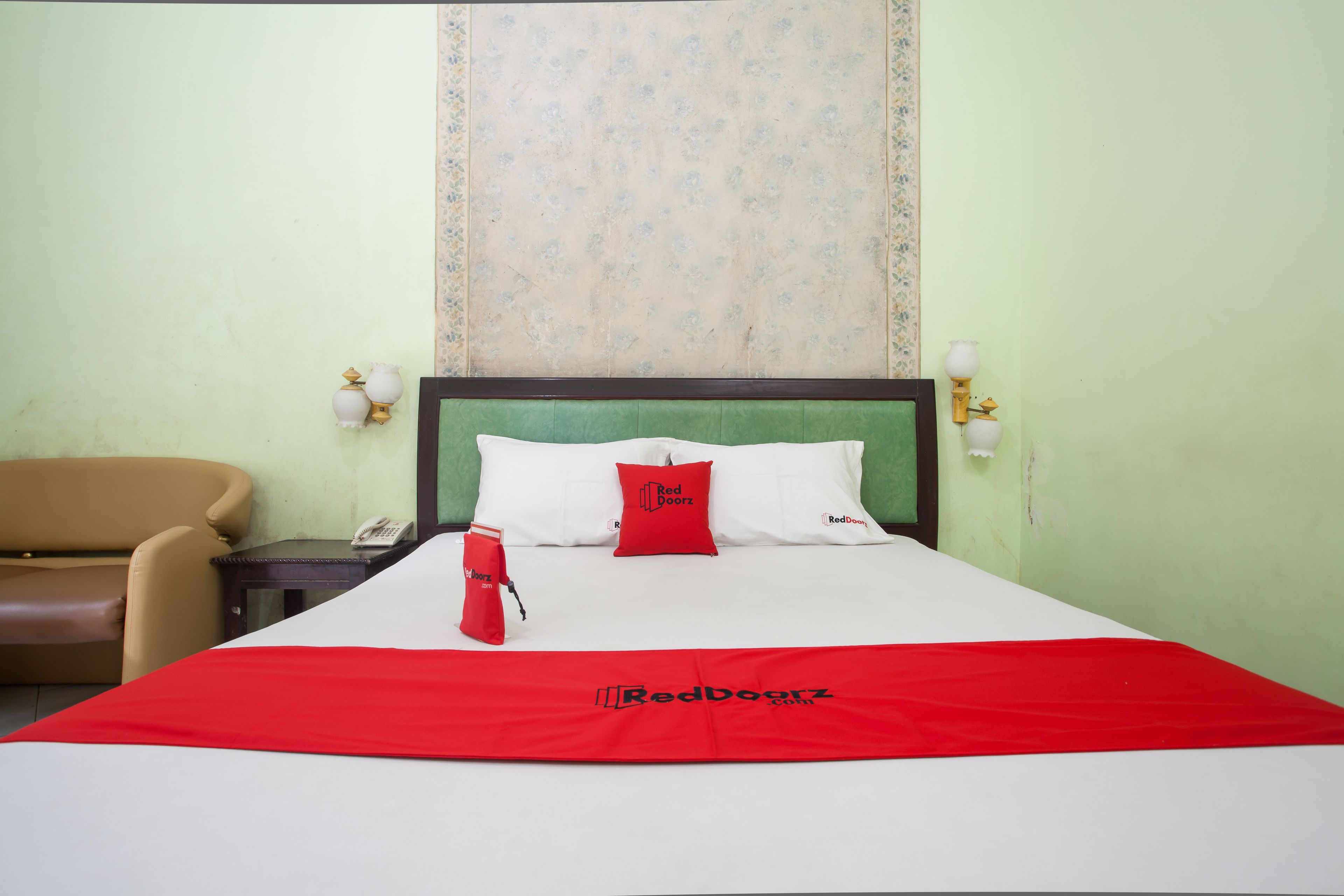 A hotel room with a bed, a nightstand, a telephone, a red throw blanket, and a red pillow.