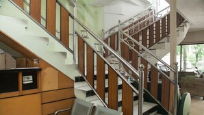 A staircase with wooden steps and metal railings, a waiting area with chairs, and a glimpse of a room with a sofa and a window. - RedDoorz near Juanda International Airport (Sidoarjo)
