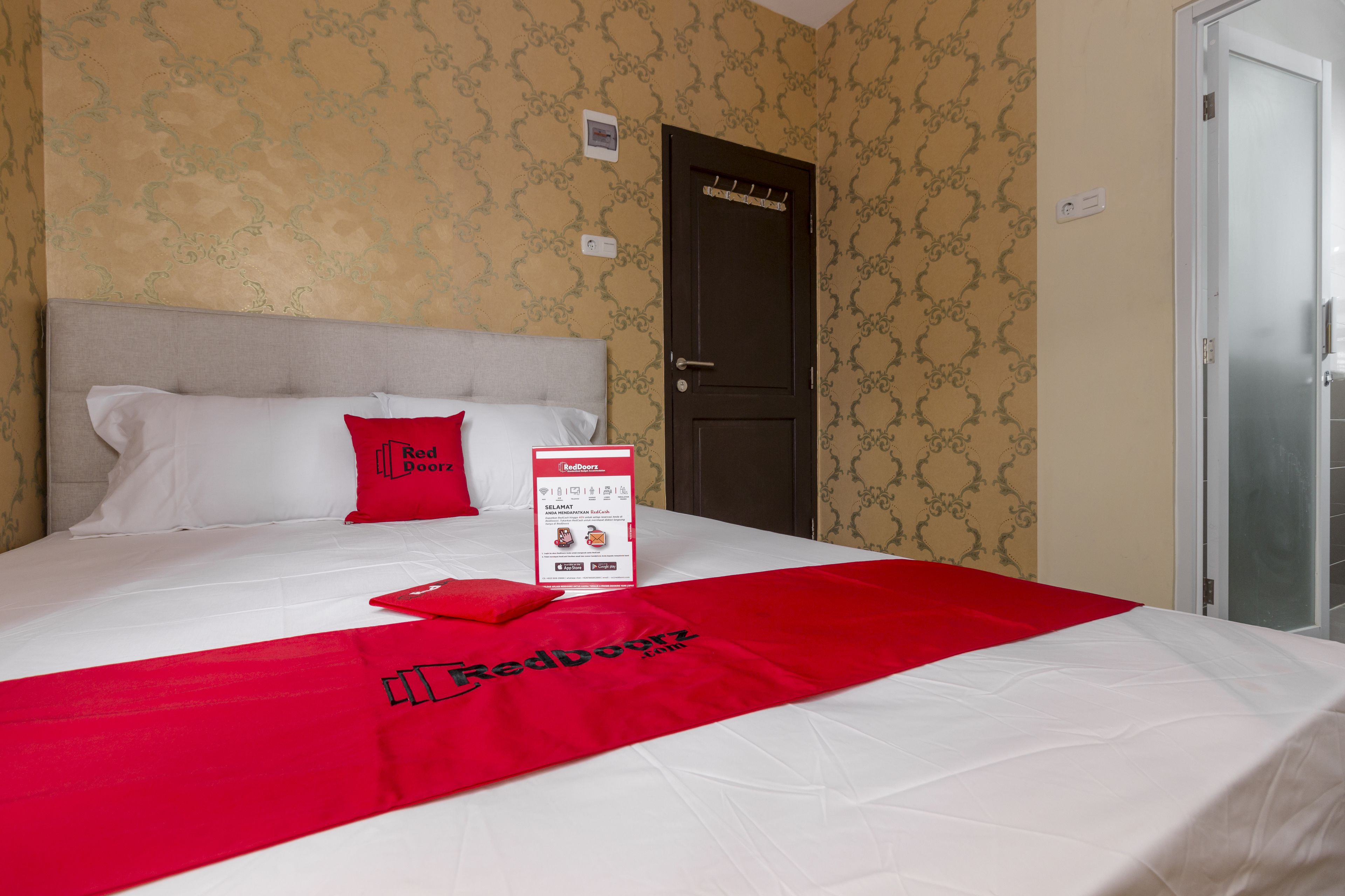 A hotel room with a bed, a red throw blanket, and a Red Door brochure on the bed.