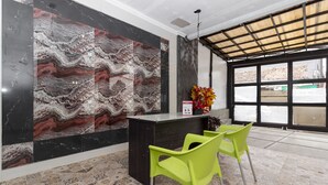 Un espace d’accueil avec un mur en marbre, un comptoir de réception, deux fauteuils verts et une grande fenêtre donnant sur l’extérieur.
