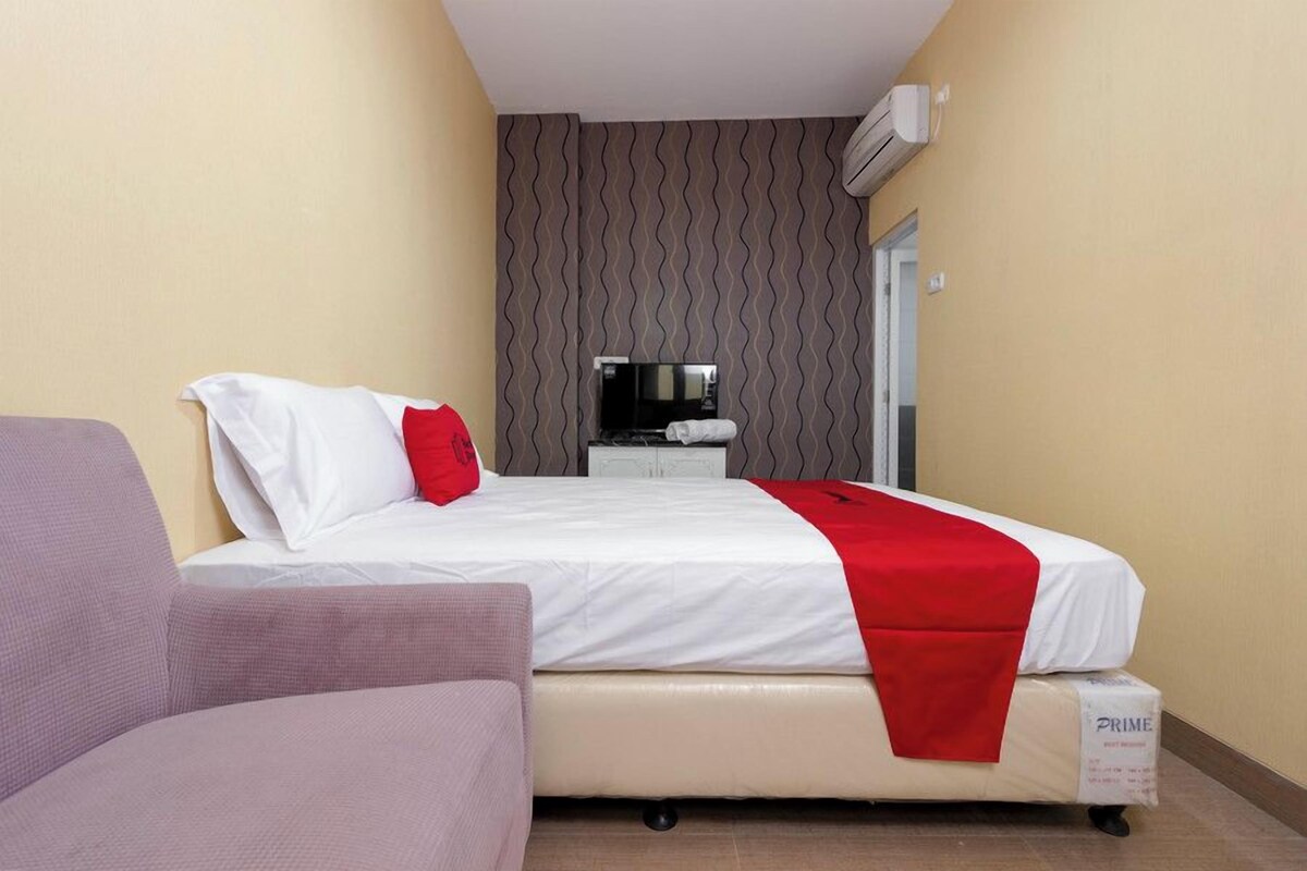 A hotel room with a bed, a bedside table, a TV, and an air conditioning unit.