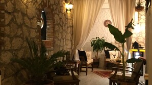 A cozy interior with stone walls, a staircase, and a seating area with chairs and potted plants. - Simira Hotel (Cesme)