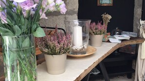A rustic wooden table with a vase of pink flowers, a glass vase with green plants, and a candle holder with dried flowers. - Simira Hotel (Cesme)