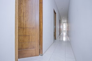 A long, narrow hallway with white walls and a wooden door on the left. - UROOMS Tanah Abang (Jakarta)