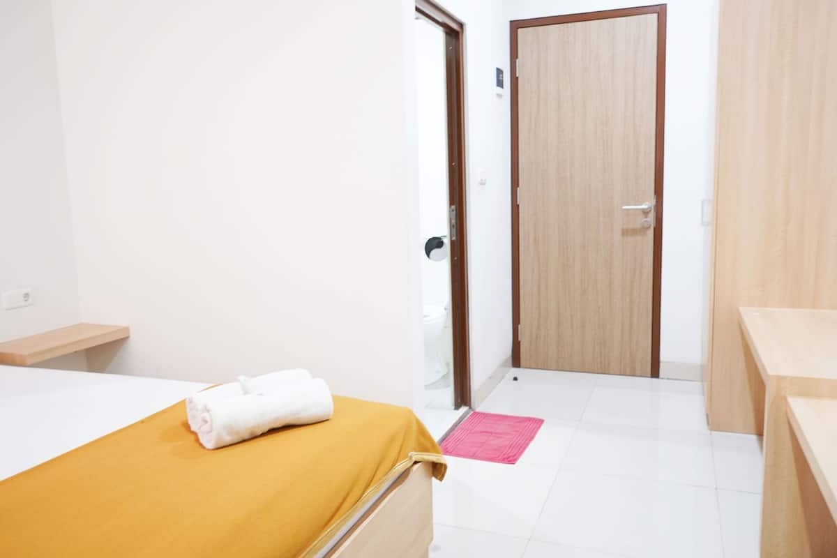 Une chambre d’hôtel avec un lit, une porte en bois, une petite table et un banc.