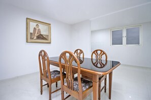 Ein Essbereich mit einem rechteckigen Tisch und vier Holzstühlen mit gepolsterten Sitzen. Ein gerahmtes Bild hängt an der Wand über dem Tisch.