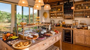 A breakfast buffet with various food items, a wine cooler, and a view of the outdoors. - Anthemion Suites & Villas (Nafplio)