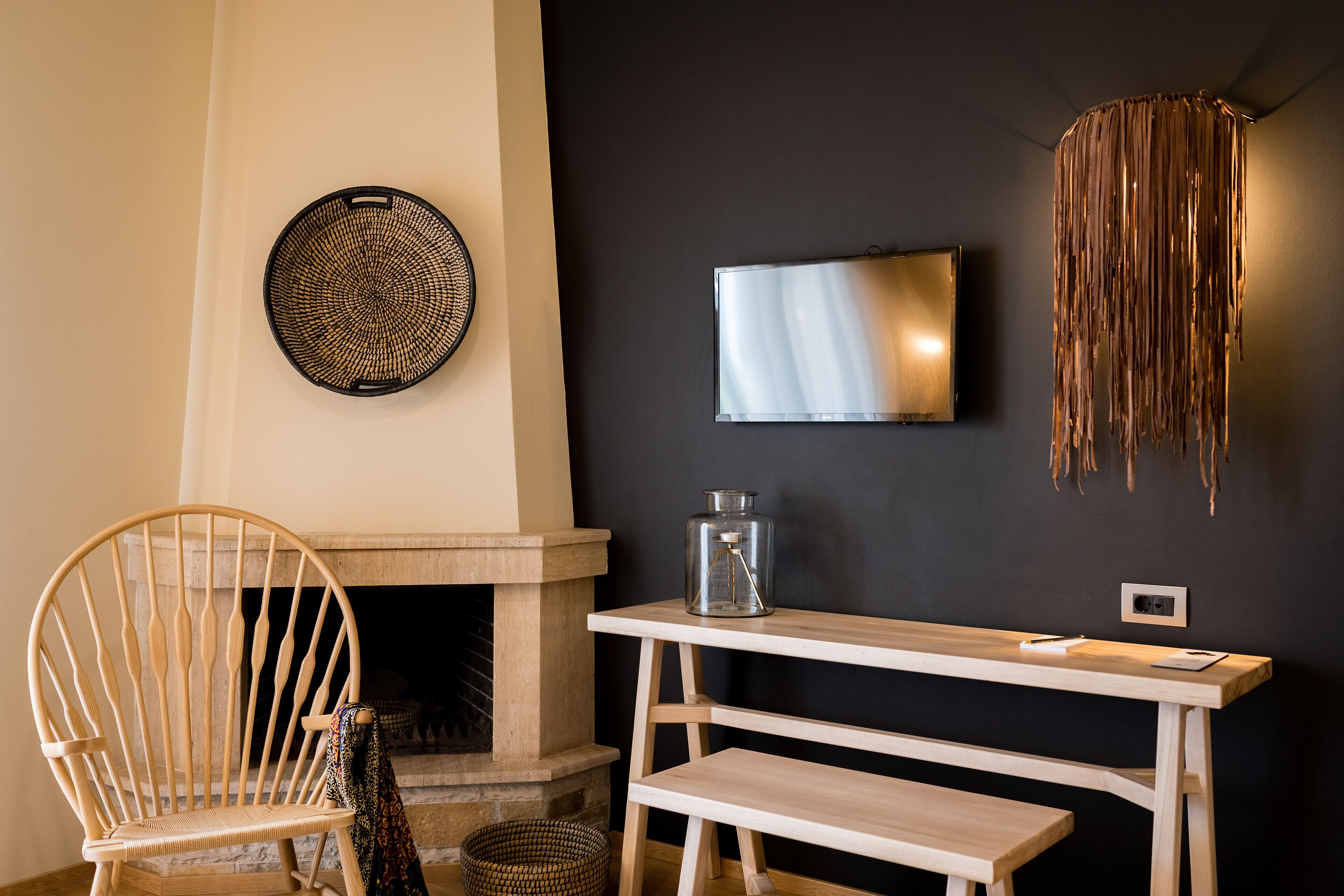 A room with a wooden chair, a fireplace, a wall-mounted TV, and a hanging light fixture.