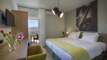 Habitación de hotel con cama, escritorio, silla, un florero con flores y vista a la ciudad.