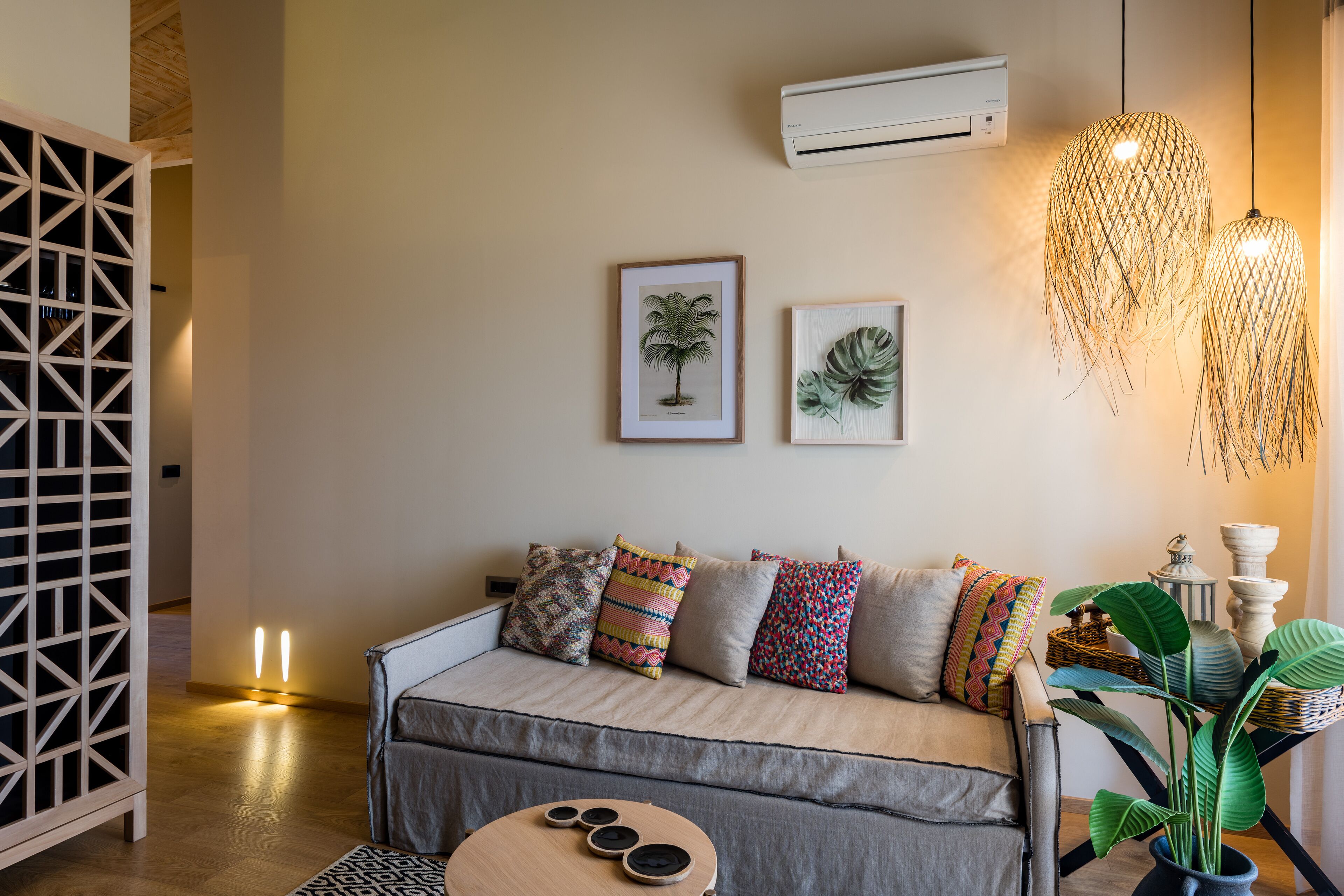 A modern living room with a sofa, colorful cushions, framed botanical prints, a hanging light fixture, and a potted plant.