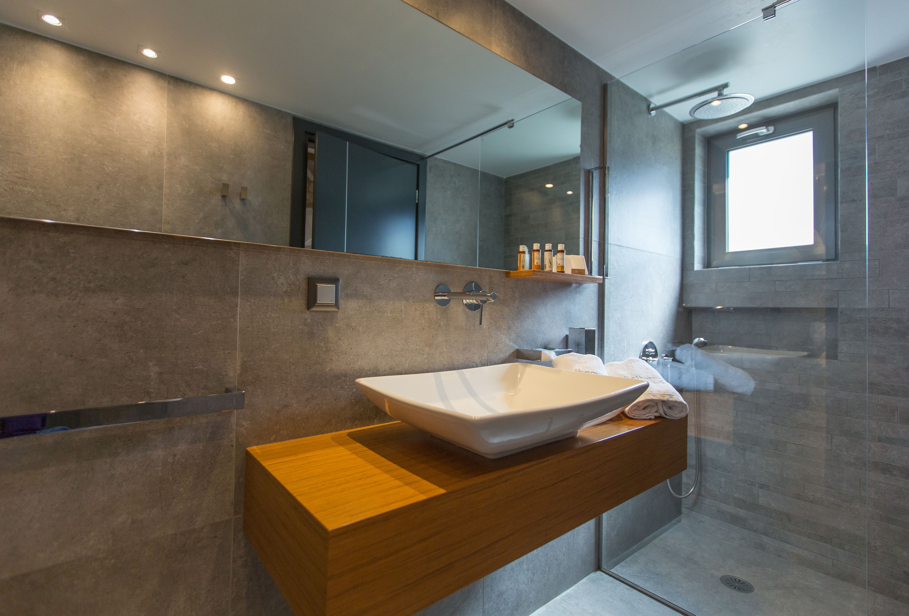 Een moderne badkamer met een grote spiegel, een houten wastafelmeubel, een witte wastafel en een douchehoek.