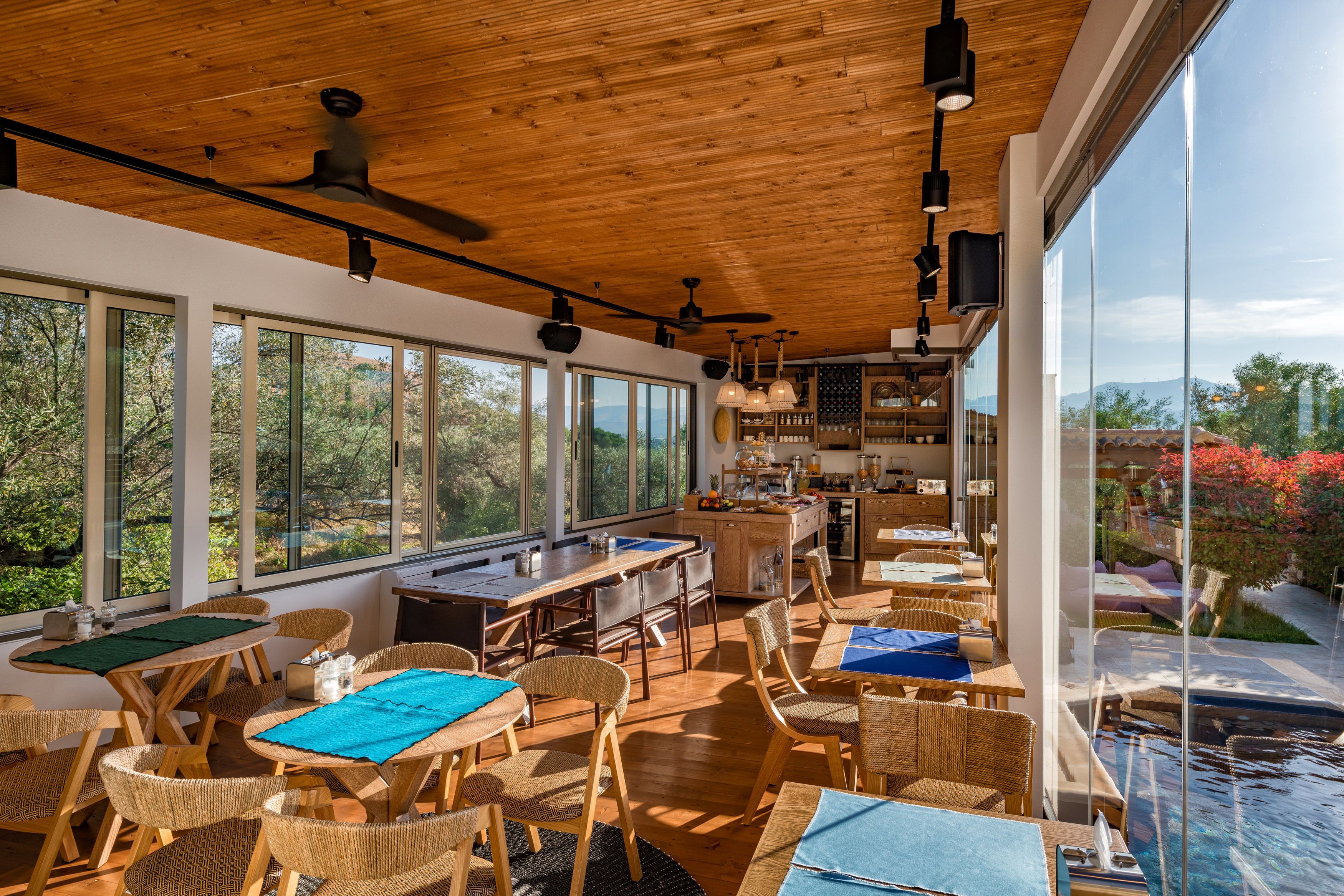 Amplio espacio interior con ventanas grandes, techo de madera y vistas a una piscina y vegetación.