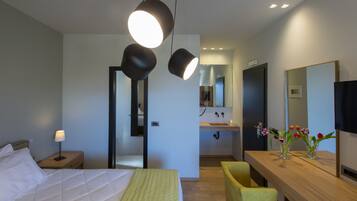 Une chambre d’hôtel moderne, équipée d’un lit, d’une table de chevet, d’une lampe et d’un bureau en bois agrémenté d’un miroir et d’un vase de fleurs.