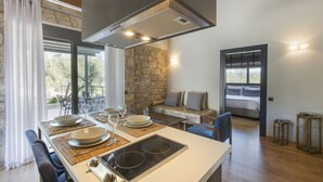 A modern kitchen with a built-in stove, dining table set for four, and a stone accent wall. - Anthemion Suites & Villas (Nafplio)