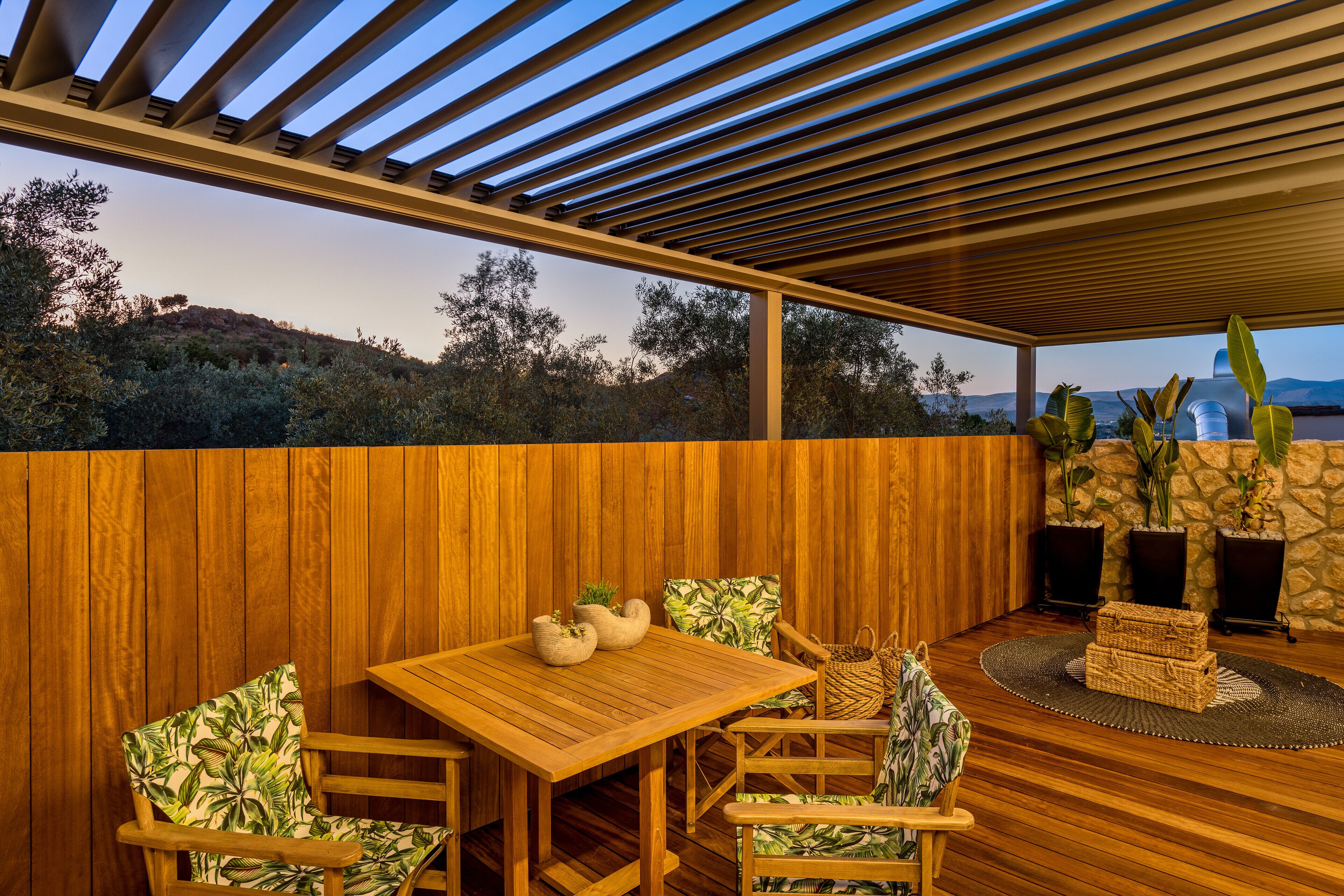 A wooden deck with a table and chairs, a stone wall, and potted plants.