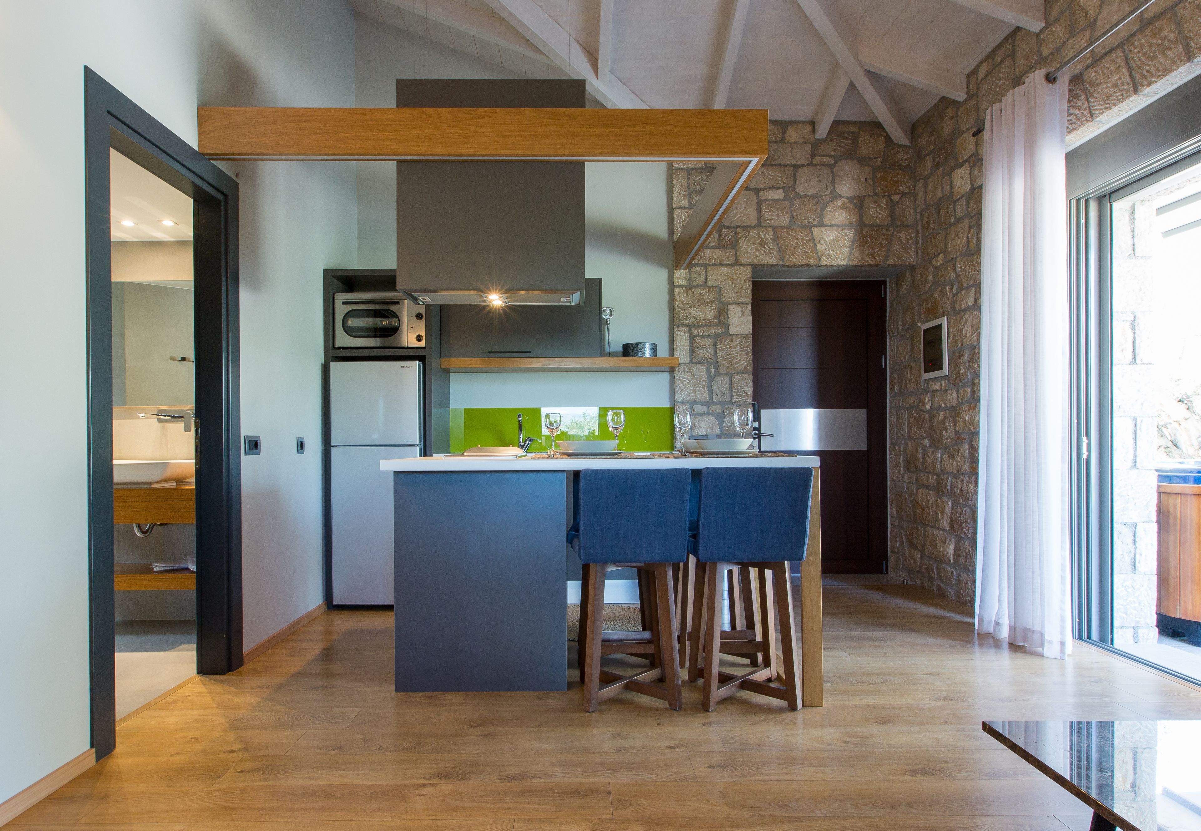 A modern kitchen with a central island, wooden stools, and a stone accent wall.