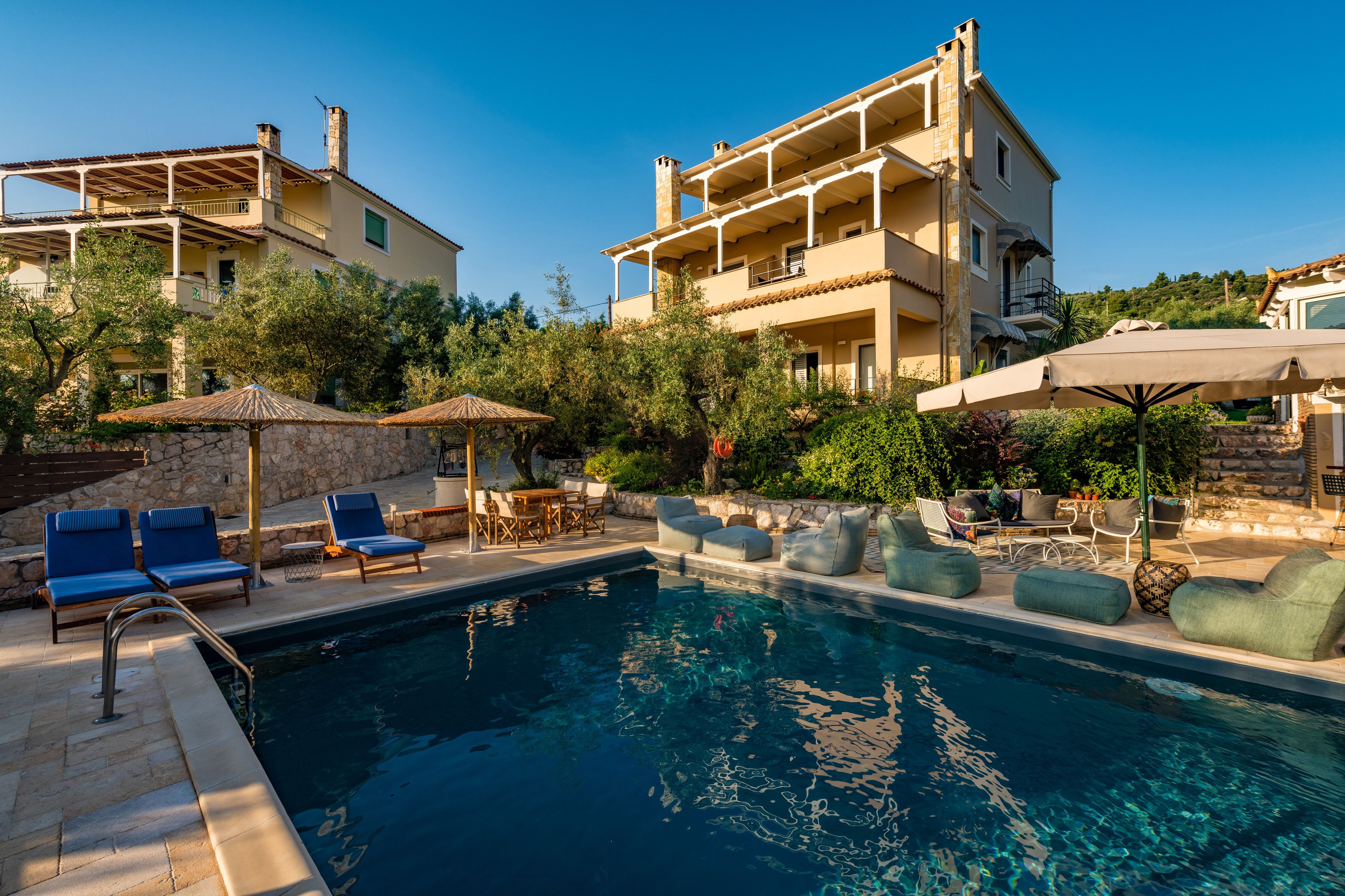 A pool area with lounge chairs and umbrellas, surrounded by stone walls and greenery.