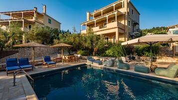 A pool area with lounge chairs and umbrellas, surrounded by stone walls and greenery.