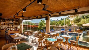 A spacious indoor area with wooden ceiling and large windows overlooking a pool and lush greenery.