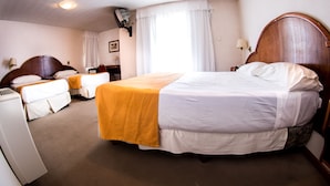 Una habitación de hotel con una cama grande, dos camas más pequeñas, un escritorio y una ventana con cortinas.
