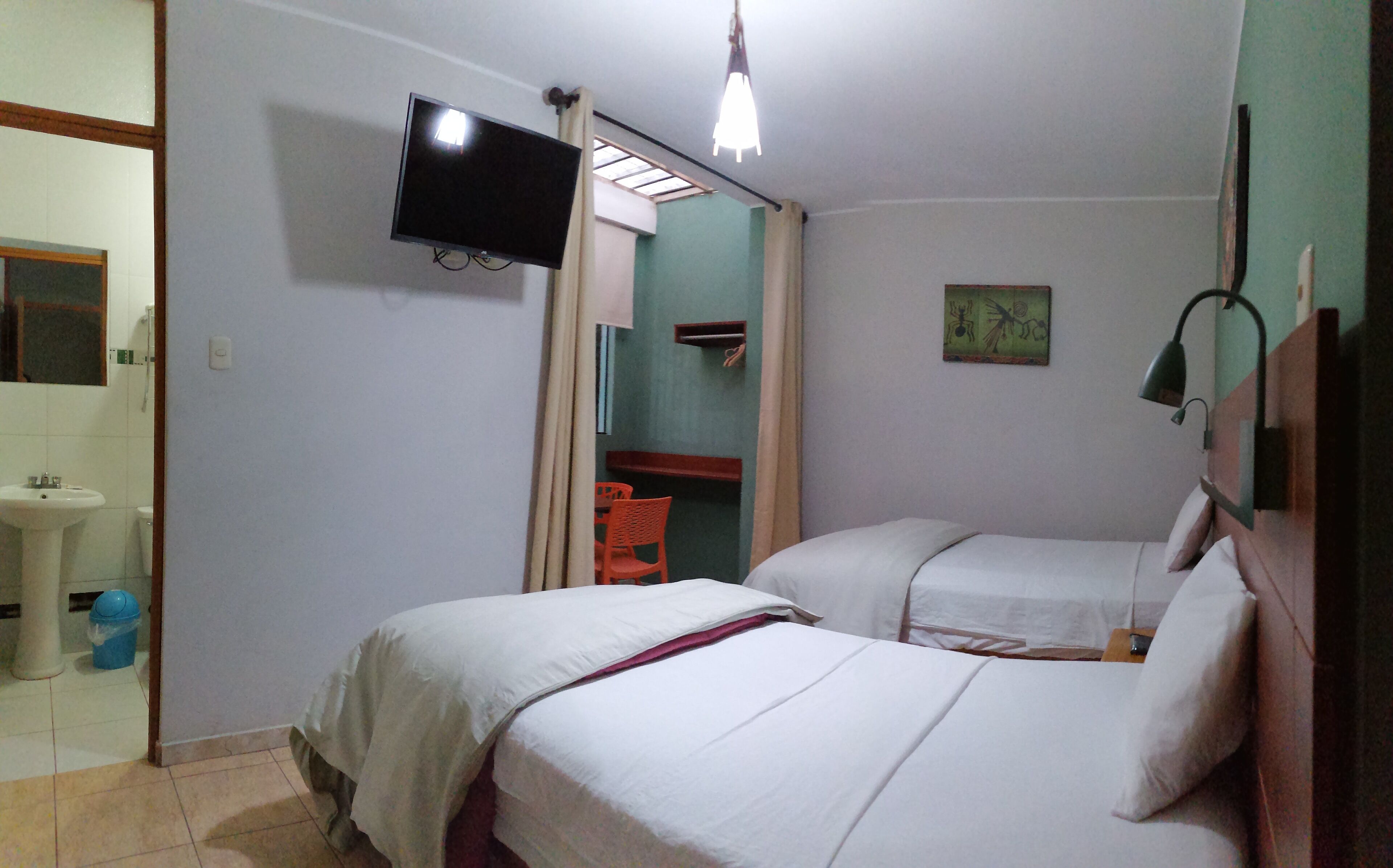 Una habitación con dos camas, televisión montada en la pared, una mesita y una silla.