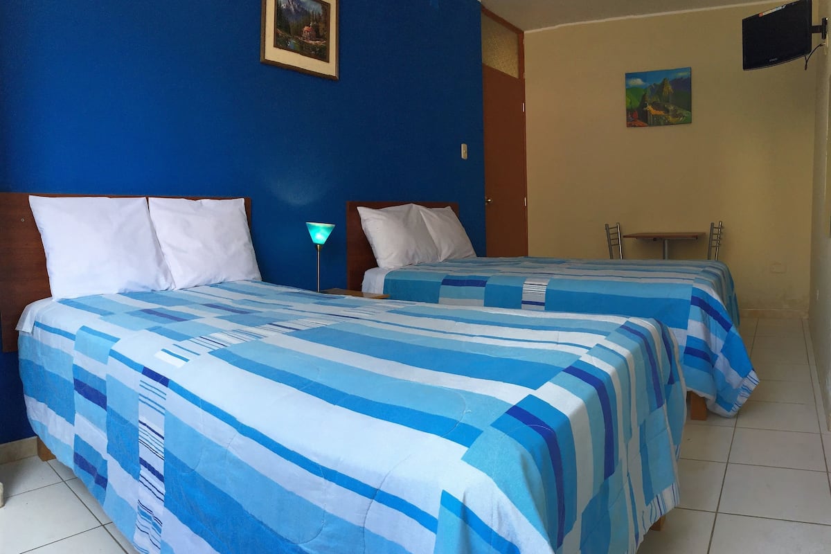 A hotel room with two beds, each with blue and white striped bedding. There is a nightstand with a lamp between the beds.